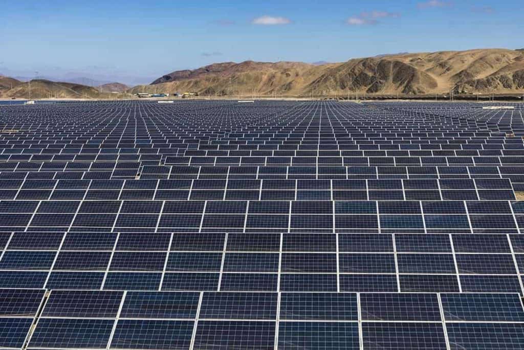 A utility-scale solar panel farm with mountains and blue sky in the background.