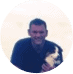 A smiling man holding a small dog, framed in a circular border against a pale background.