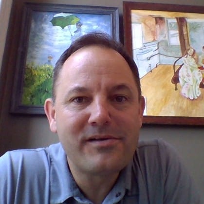 A smiling person posing for a selfie with colorful artwork on the wall in the background.