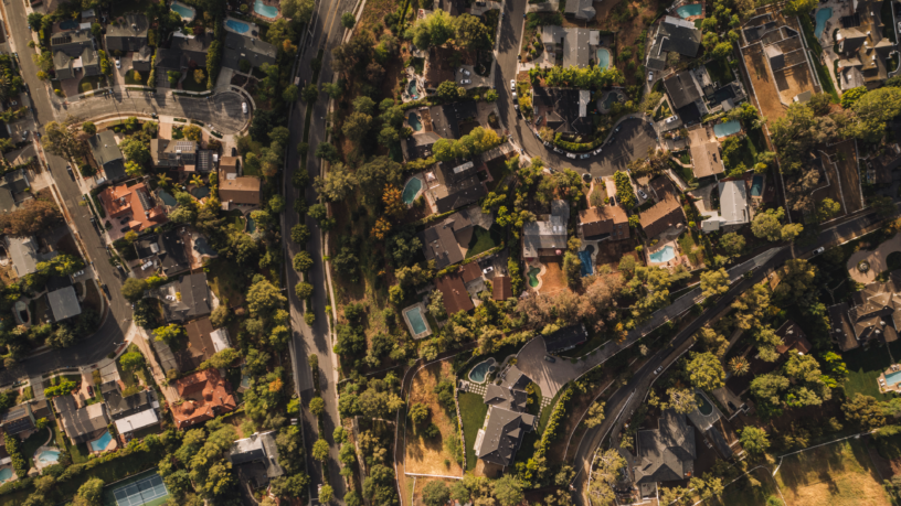 Aerial view of a residential area showing a tapestry of houses, pools, and winding streets amidst a canopy of trees.